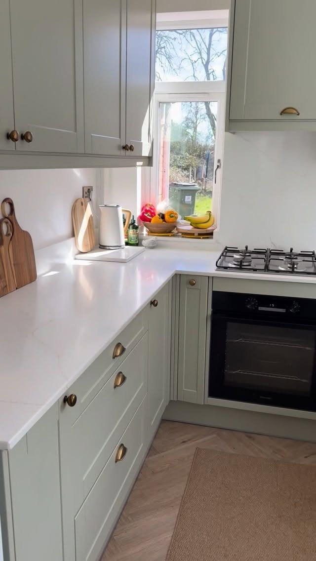 Sage green farmhouse kitchen cabinets with gold hardware and white countertops.