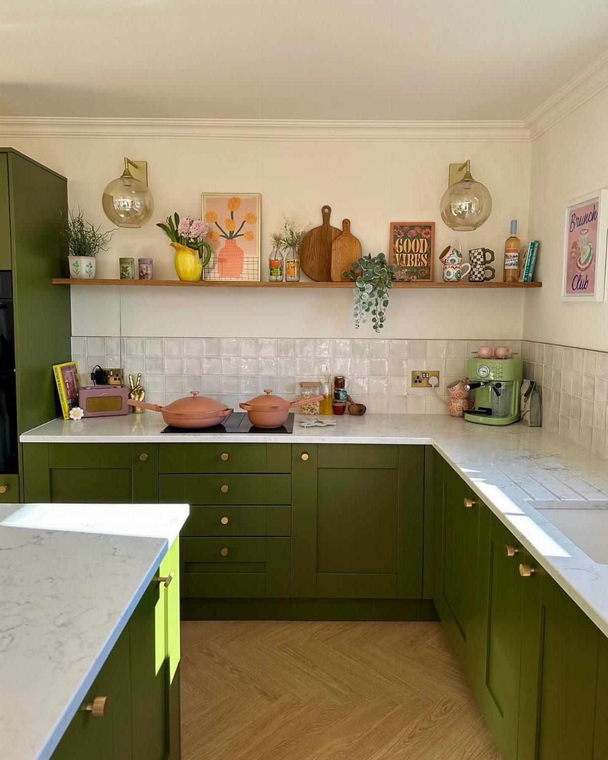 Olive green kitchen cabinets with a wooden open shelf displaying farmhouse decor items.