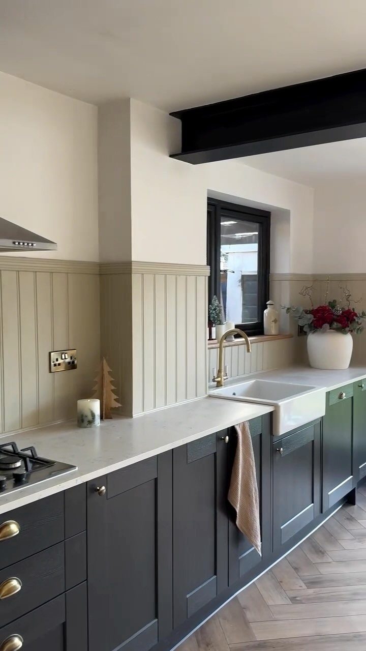 Beige beadboard backsplash in a farmhouse kitchen with dark grey cabinets and white counters.