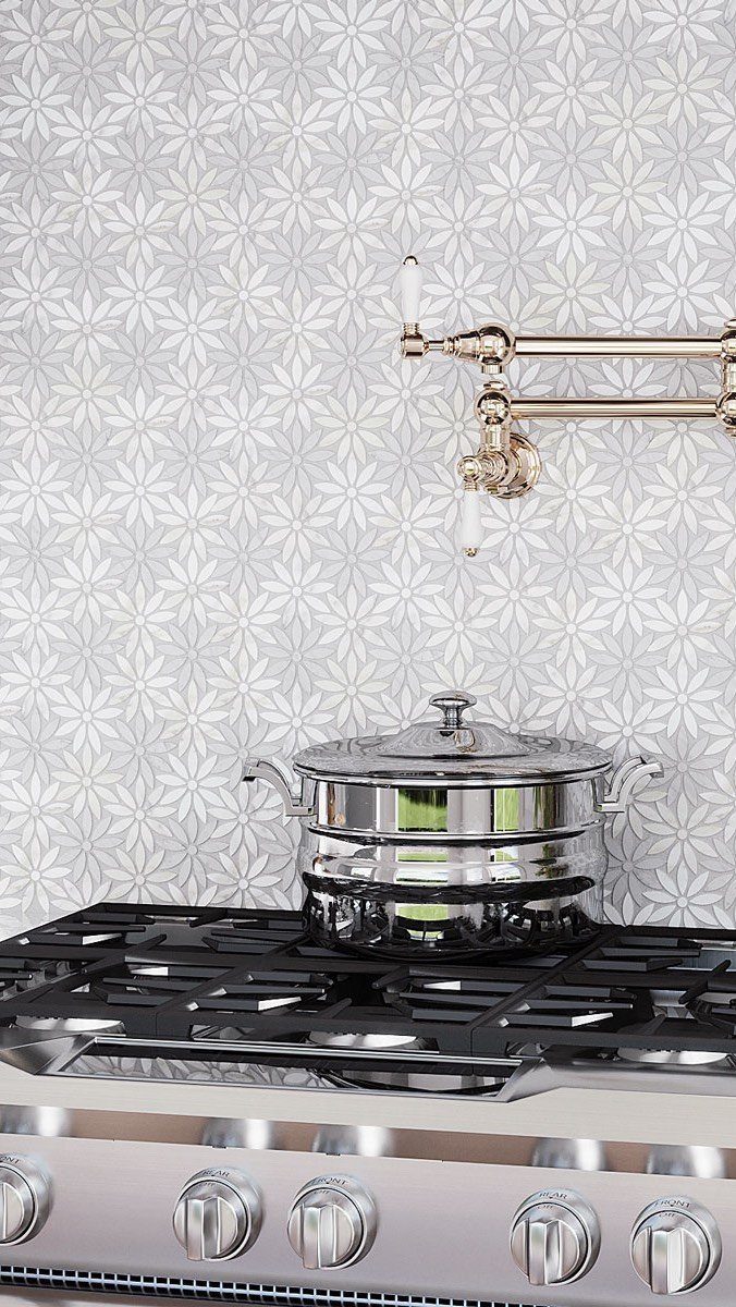 Floral patterned ceramic tile backsplash behind a stainless steel stove and gold faucet.