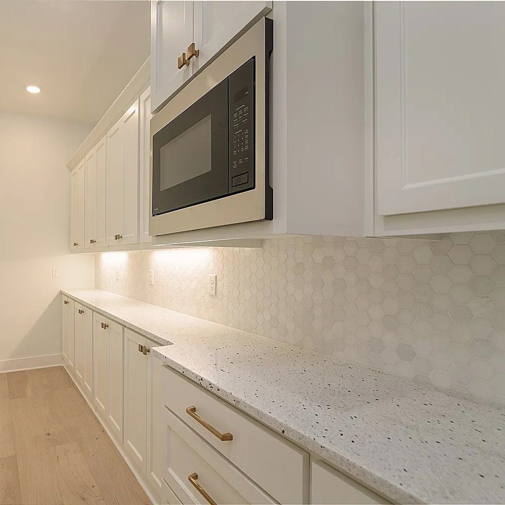 White hexagonal tile backsplash in a bright kitchen with white cabinets and quartz countertops