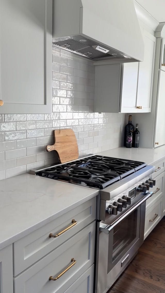 White subway tile backsplash in a kitchen with grey cabinets and stainless steel stove
