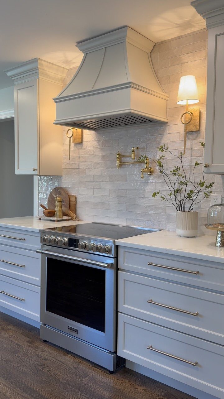 White farmhouse kitchen with textured tile backsplash, white cabinets, and gold wall sconces.