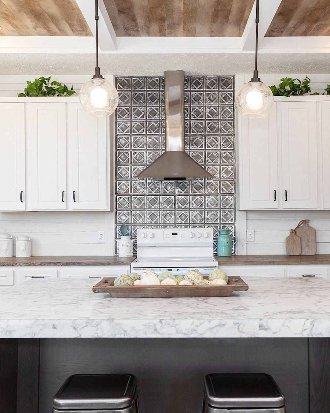 Metallic patterned tile backsplash in a white farmhouse kitchen with marble countertops.