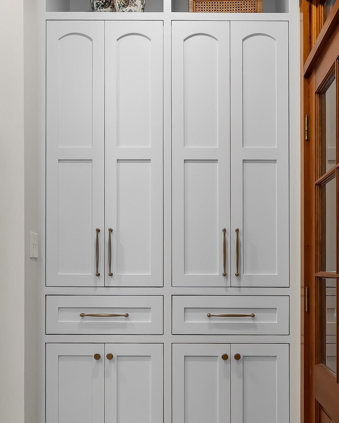 White floor to ceiling cabinets with arched panels and gold hardware in a room.