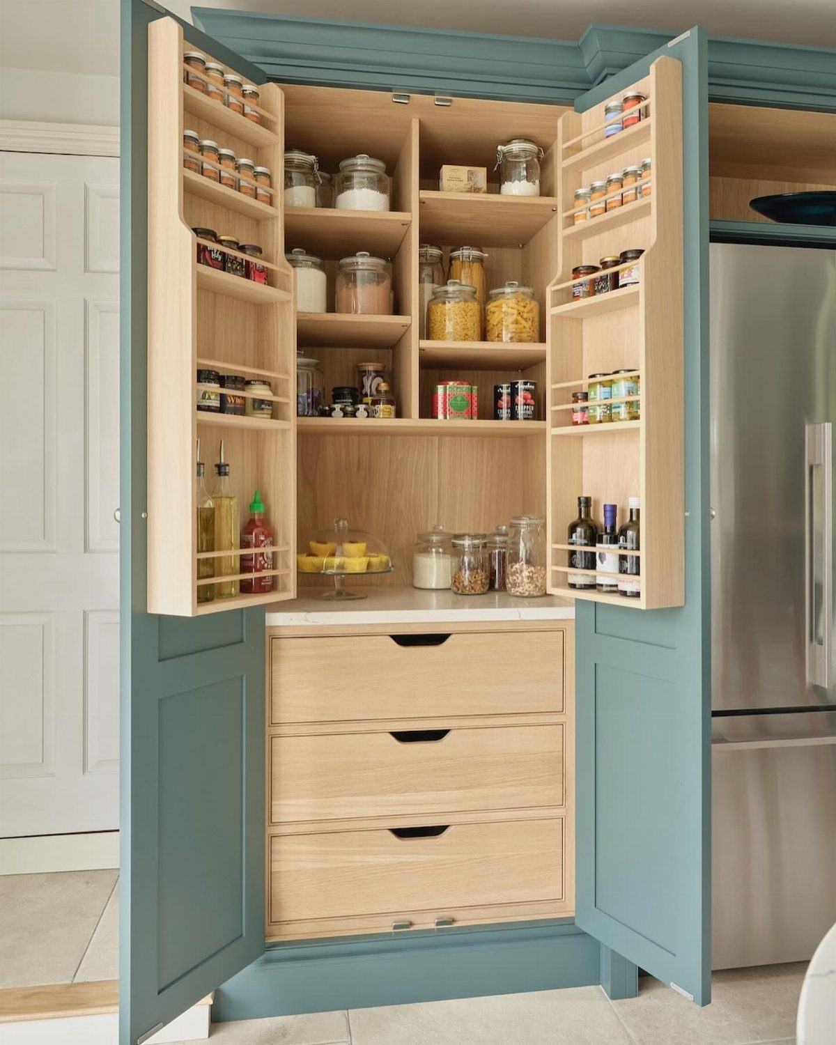 Blue floor to ceiling pantry cabinet with light wood interior shelves and drawers