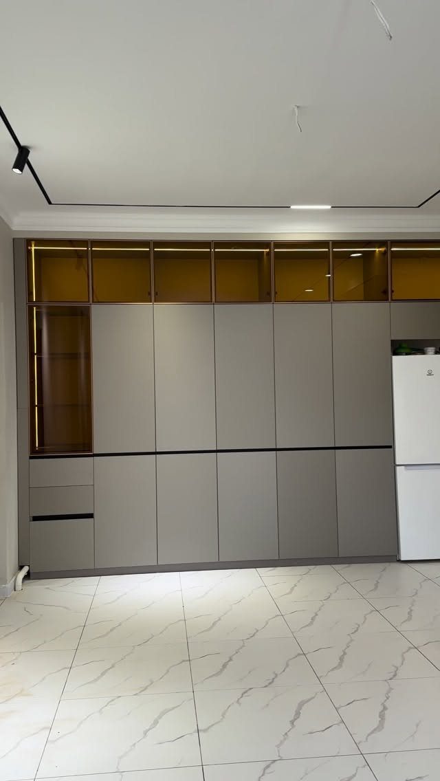 Grey floor-to-ceiling kitchen cabinets with glass upper panels and a white refrigerator.
