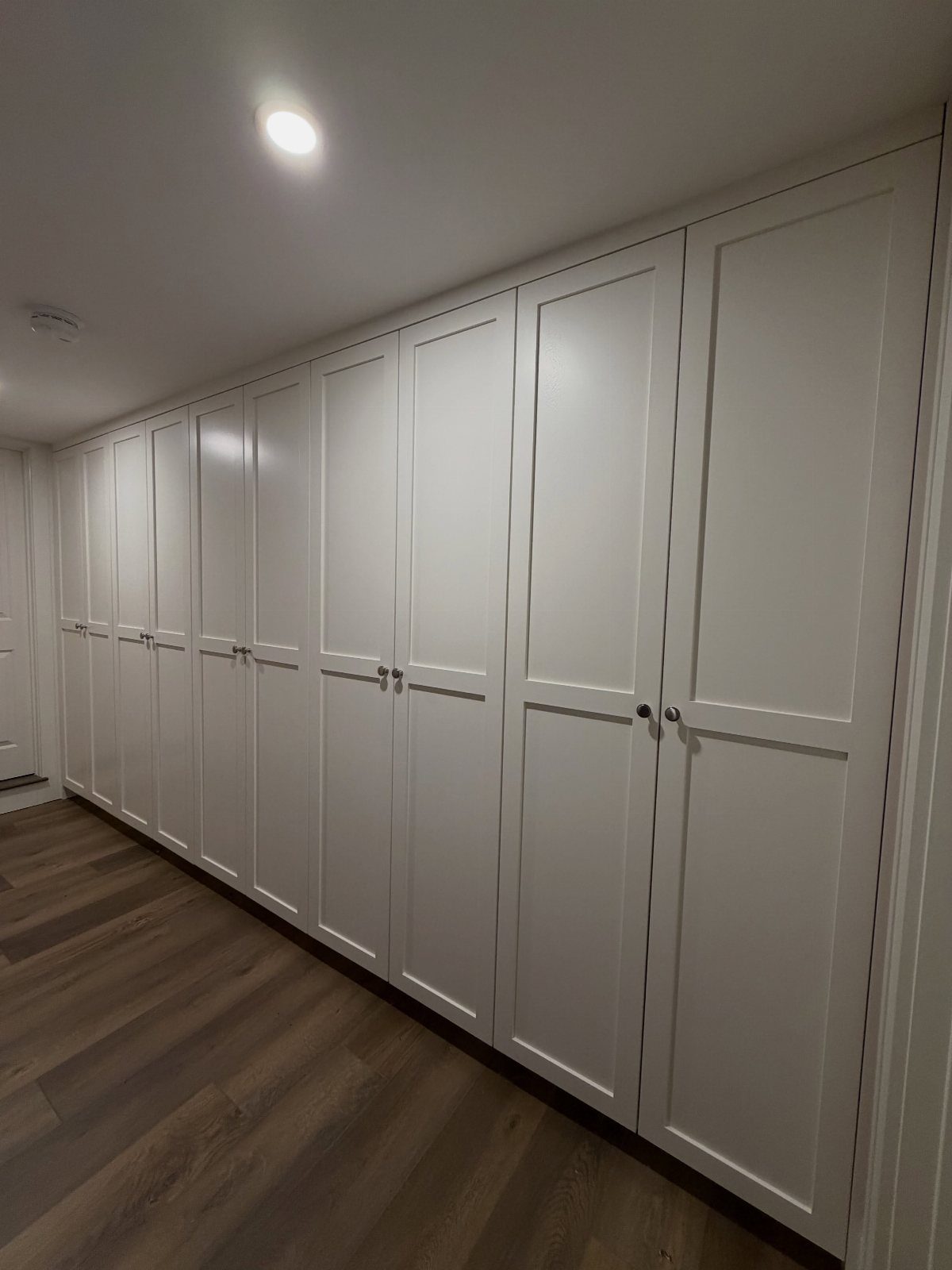 White floor to ceiling built-in cabinets with silver knobs and wood flooring.