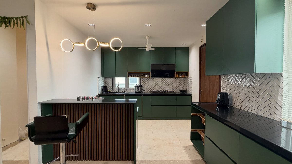 Forest green kitchen cabinets with black countertops and a white herringbone backsplash.