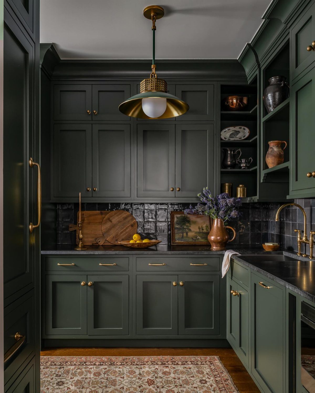 Dark green kitchen cabinets with gold hardware and a black tiled backsplash.