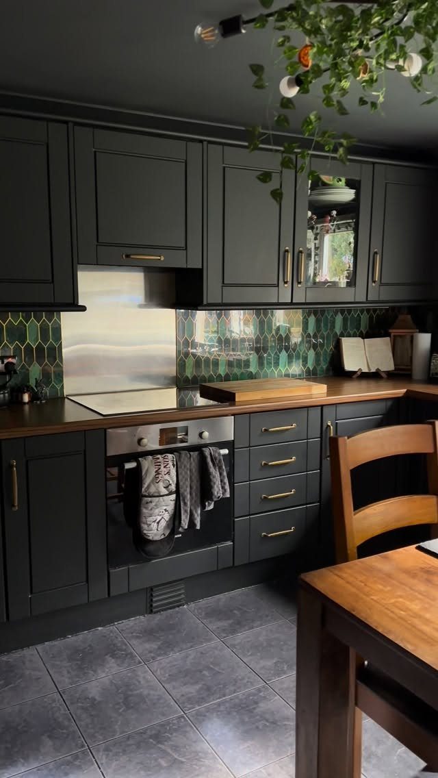 Deep green kitchen cabinets with gold hardware and a green hexagonal tile backsplash.