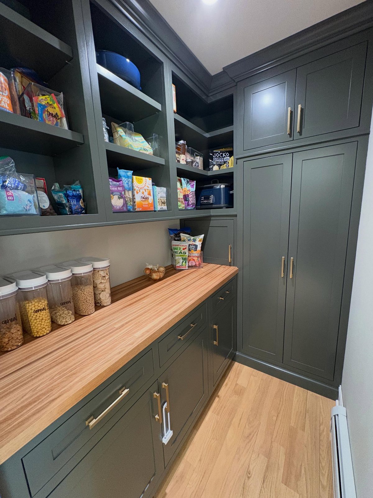 Dark green pantry cabinets with a light wood butcher block countertop and shelving