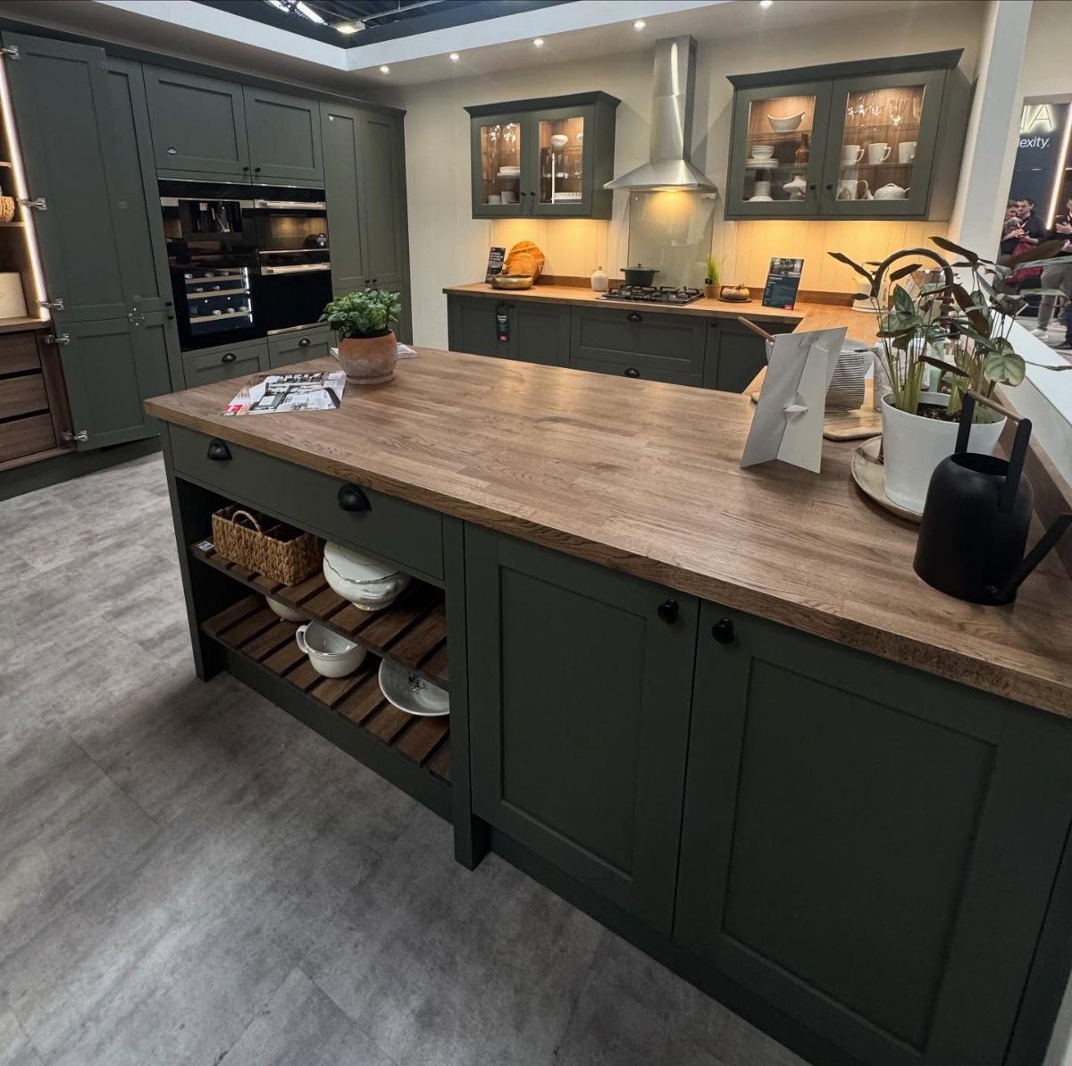 Dark green kitchen cabinets and island with a thick wooden butcher block countertop.