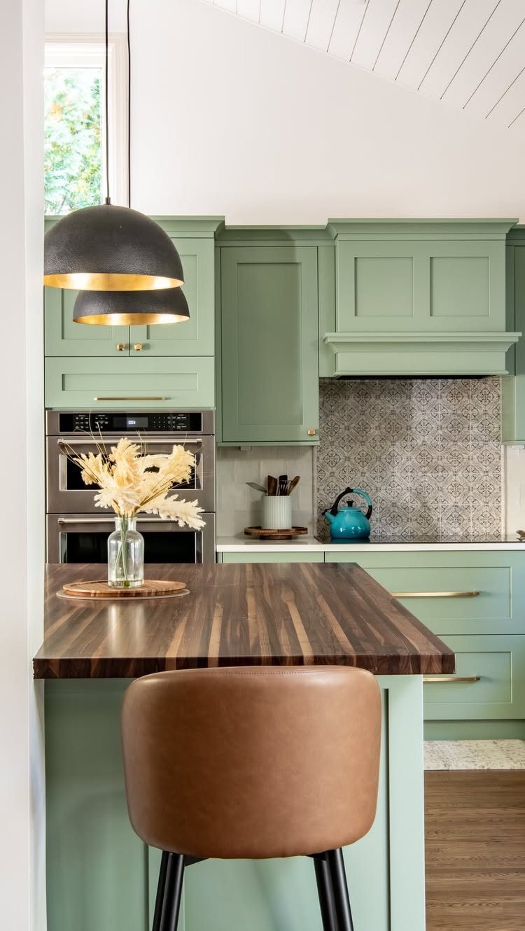 Olive green kitchen cabinets with dark walnut butcher block countertops and gold hardware.
