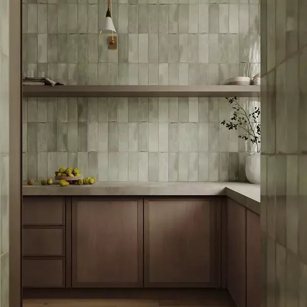 Sage green subway tiles arranged vertically as a kitchen backsplash with wooden cabinets.
