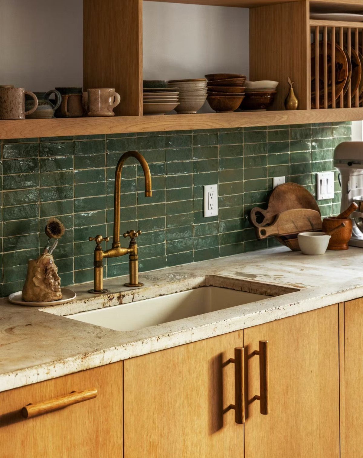 Dark green glossy subway tile backsplash with brass faucet and light wood cabinets.