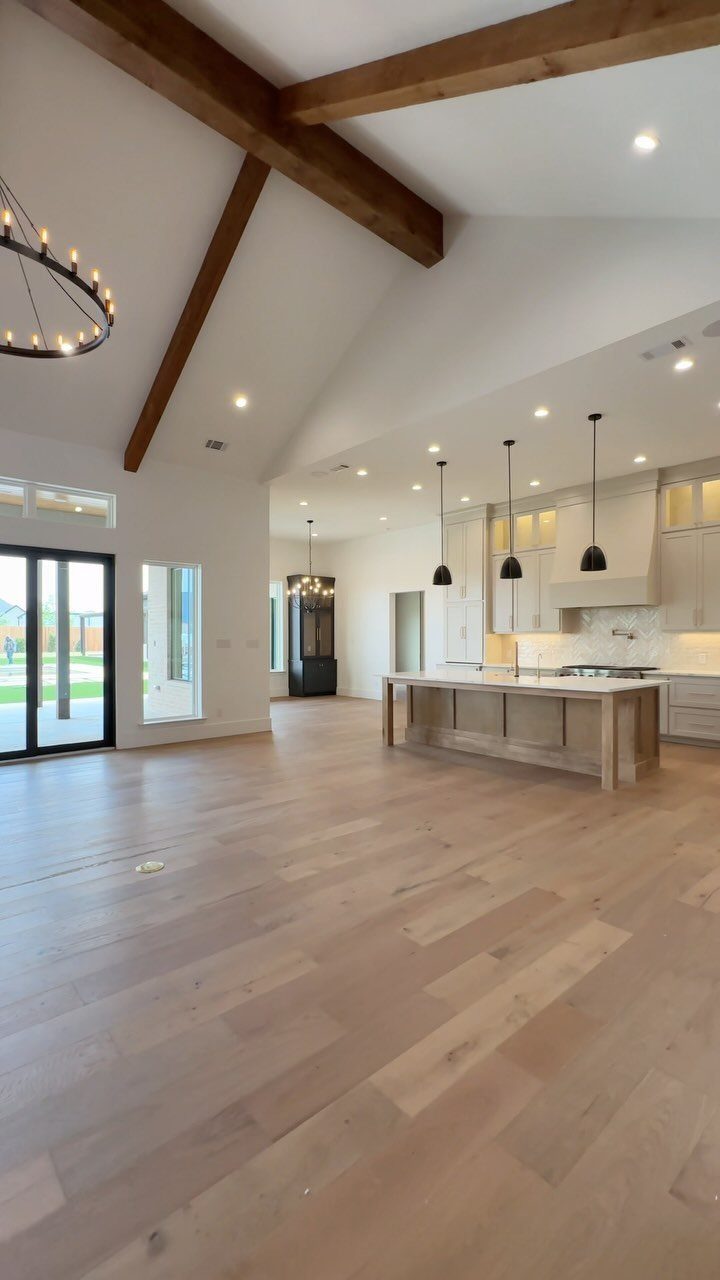 Modern kitchen with light wood floors, white cabinets, and multiple black pendant lights.