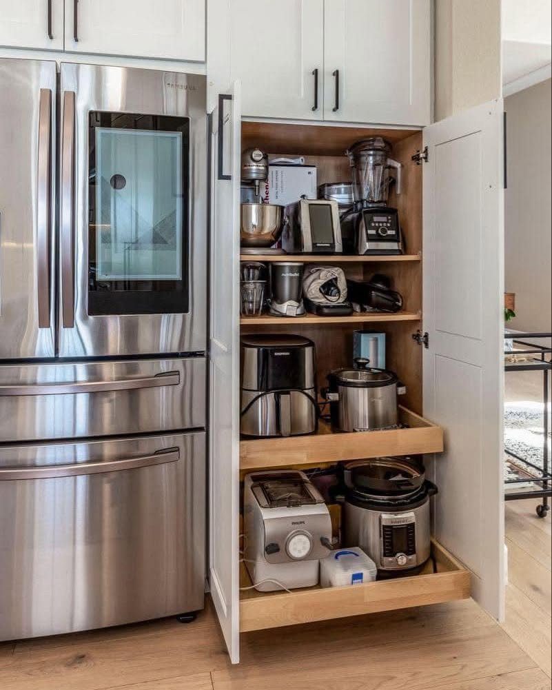 White kitchen cabinet appliance garage with wooden shelves holding various small kitchen appliances.