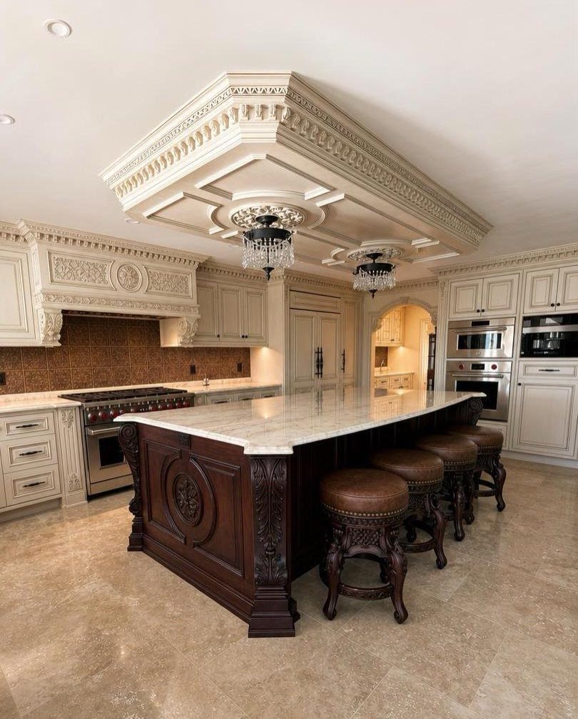 Ornate coffered ceiling with crystal chandeliers above a luxury kitchen island and cabinetry.