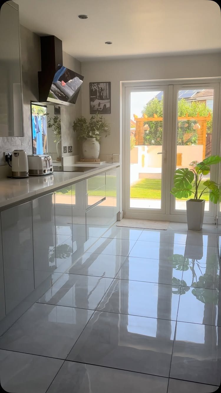 Modern white kitchen with large glass doors opening to a sunny outdoor garden.