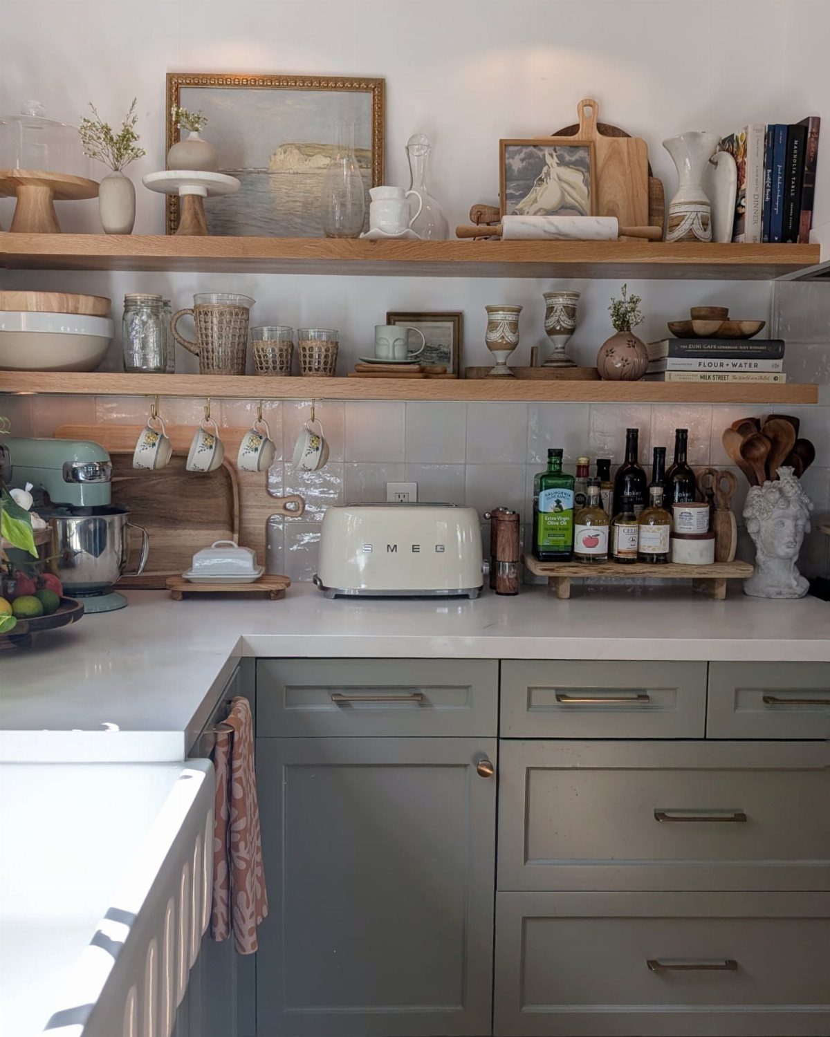 Wooden open shelves in a kitchen holding various ceramics, glassware, and cookbooks.