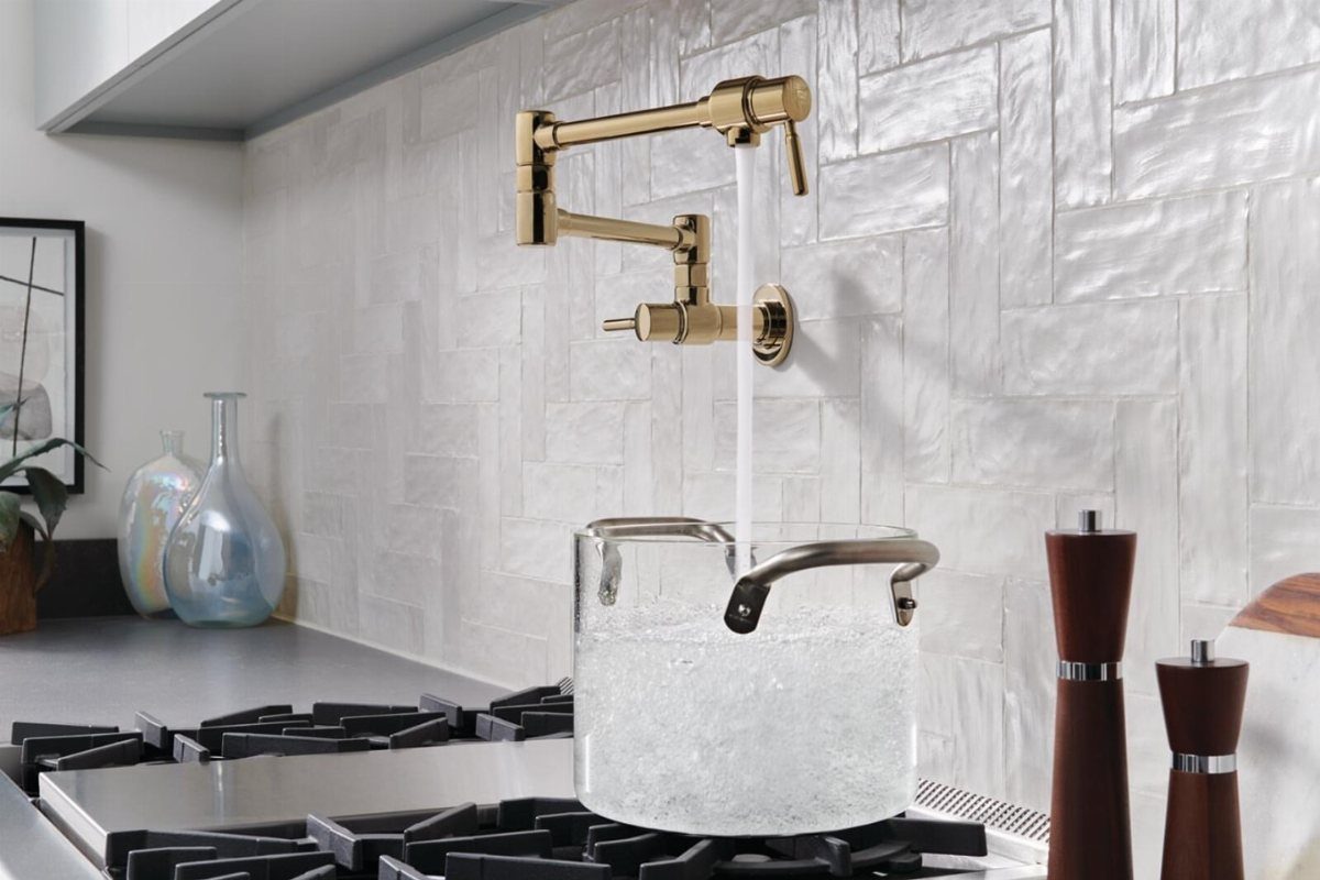 Gold pot filler faucet pouring water into a glass pot on a stovetop