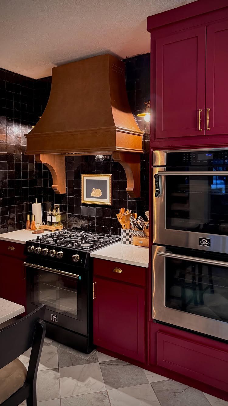 Magenta kitchen cabinets with a copper range hood and stainless steel double ovens.