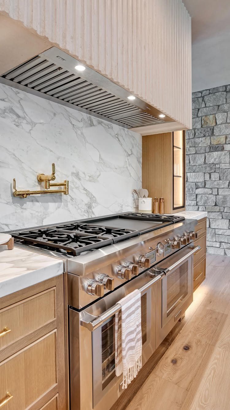 Fluted white range hood above a professional stainless steel stove and marble backsplash.