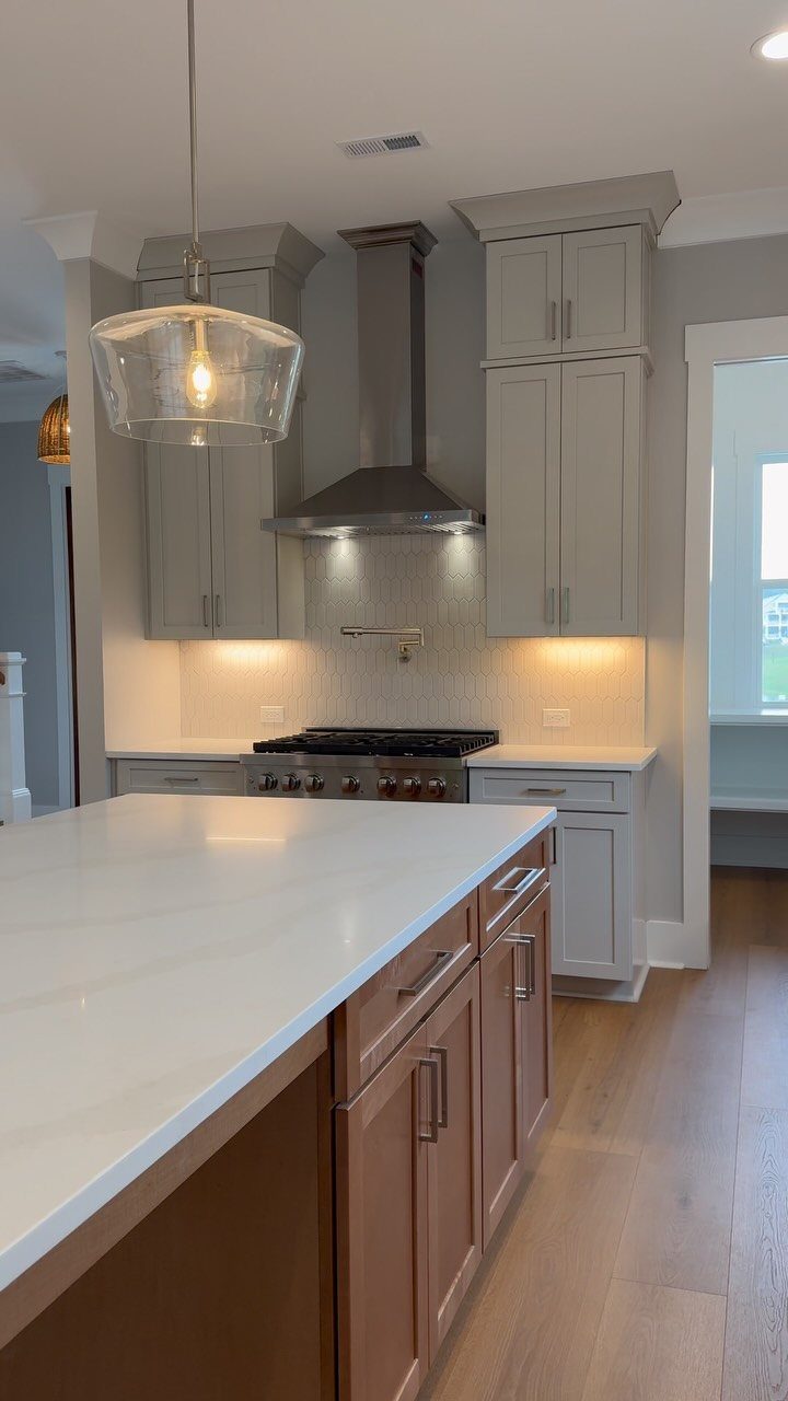 Grey perimeter cabinets and a wood-toned kitchen island with white marble countertops.