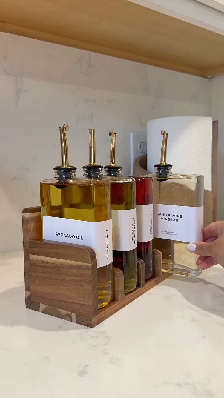 Glass oil and vinegar bottles with white labels in a wooden holder.
