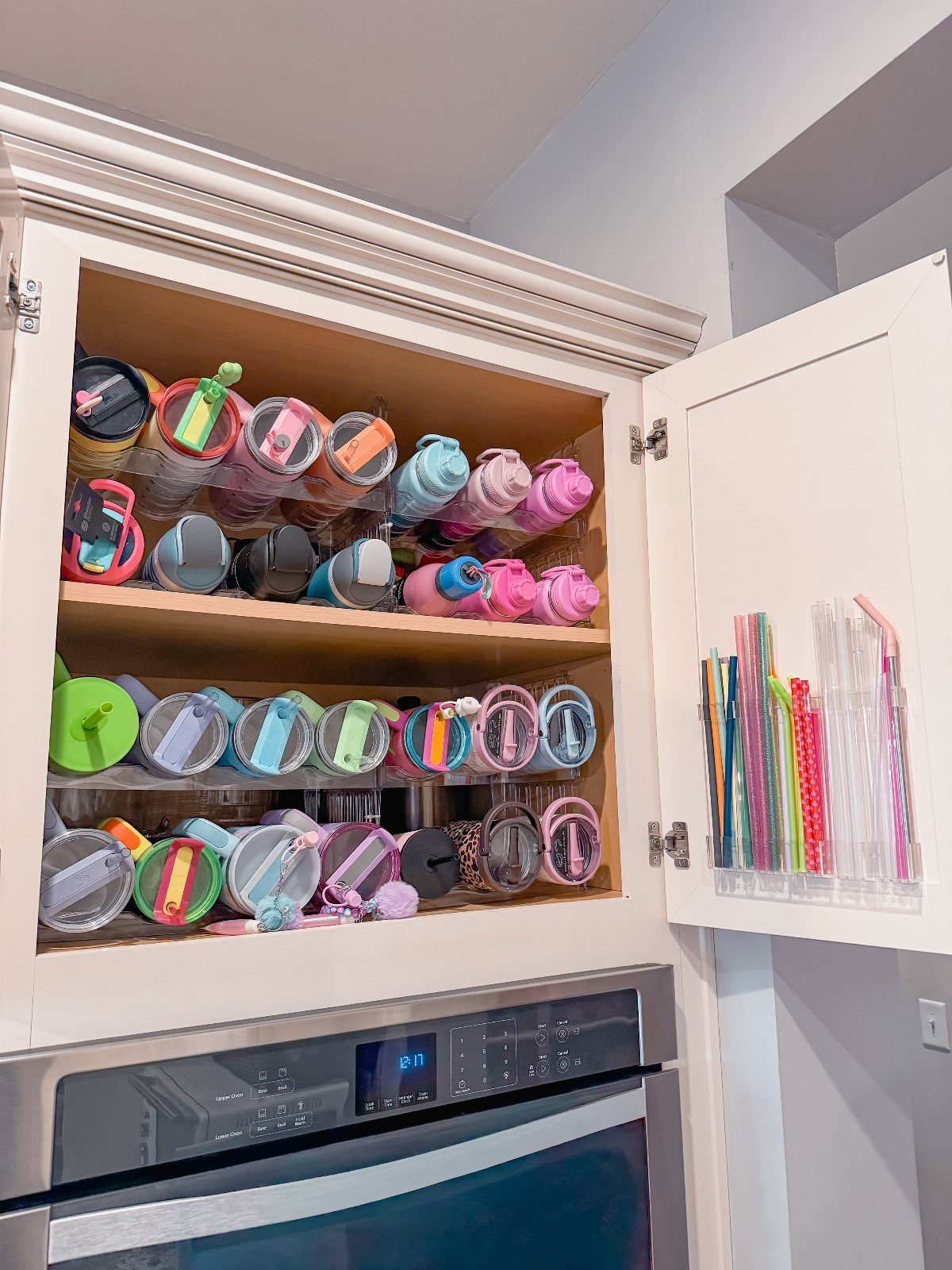 Colorful reusable cups and tumblers organized on white kitchen cabinet shelves with straws.