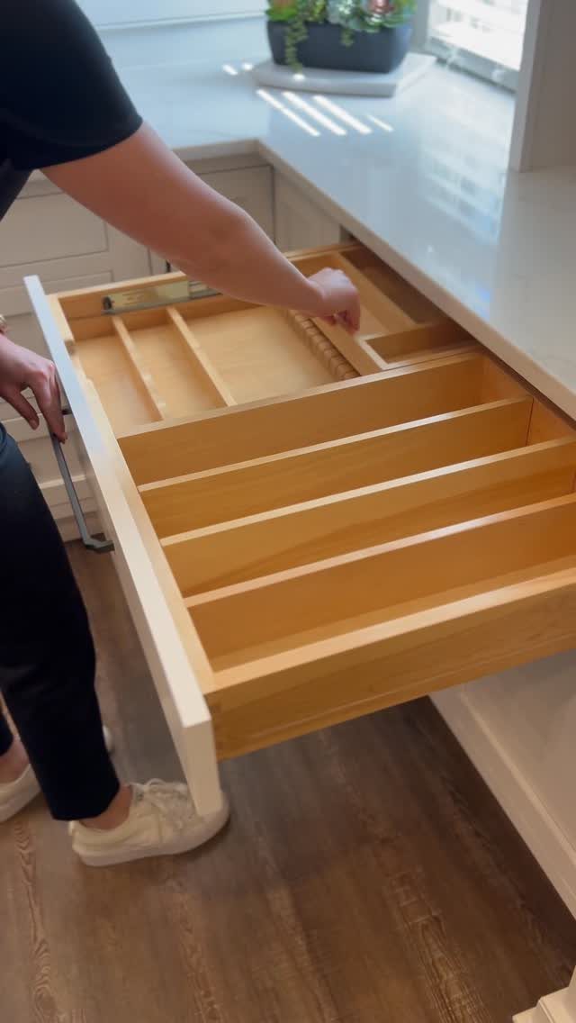 Open wooden kitchen drawer with built-in dividers under a white countertop.