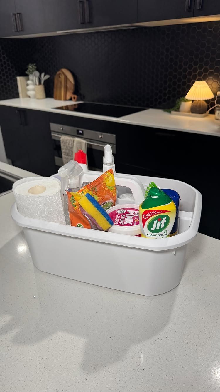 White cleaning caddy with spray bottles and sponges on a white kitchen counter.