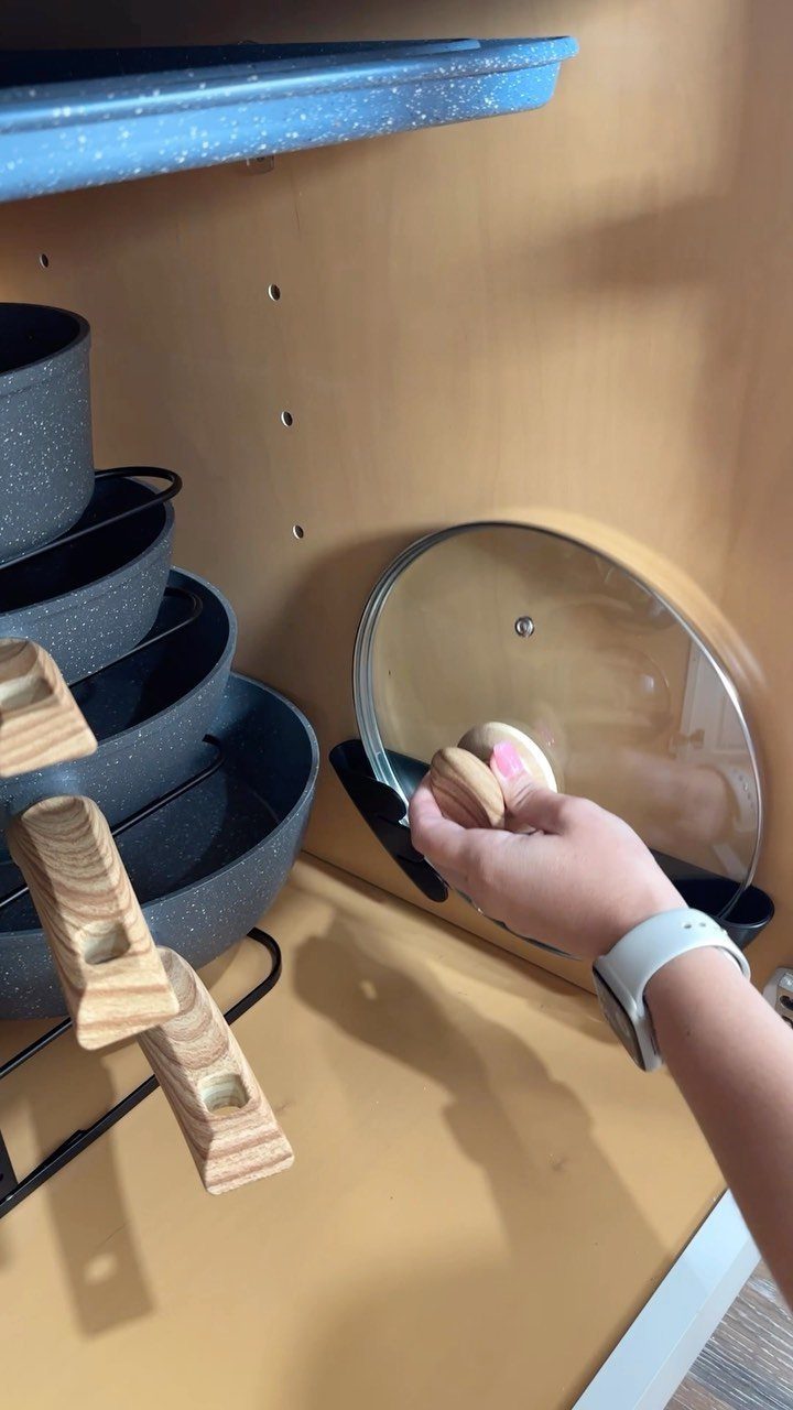 Glass lid in a black organizer inside a tan kitchen cabinet with pots.