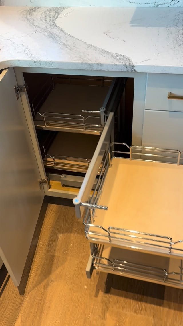 Open grey kitchen cabinet with pull-out sliding drawers and chrome metal rails.