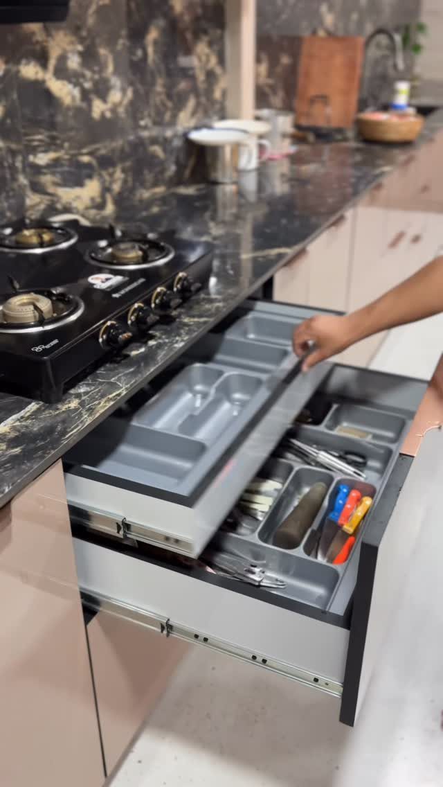 Tiered kitchen drawer pullout with grey organizers holding cutlery and kitchen utensils.