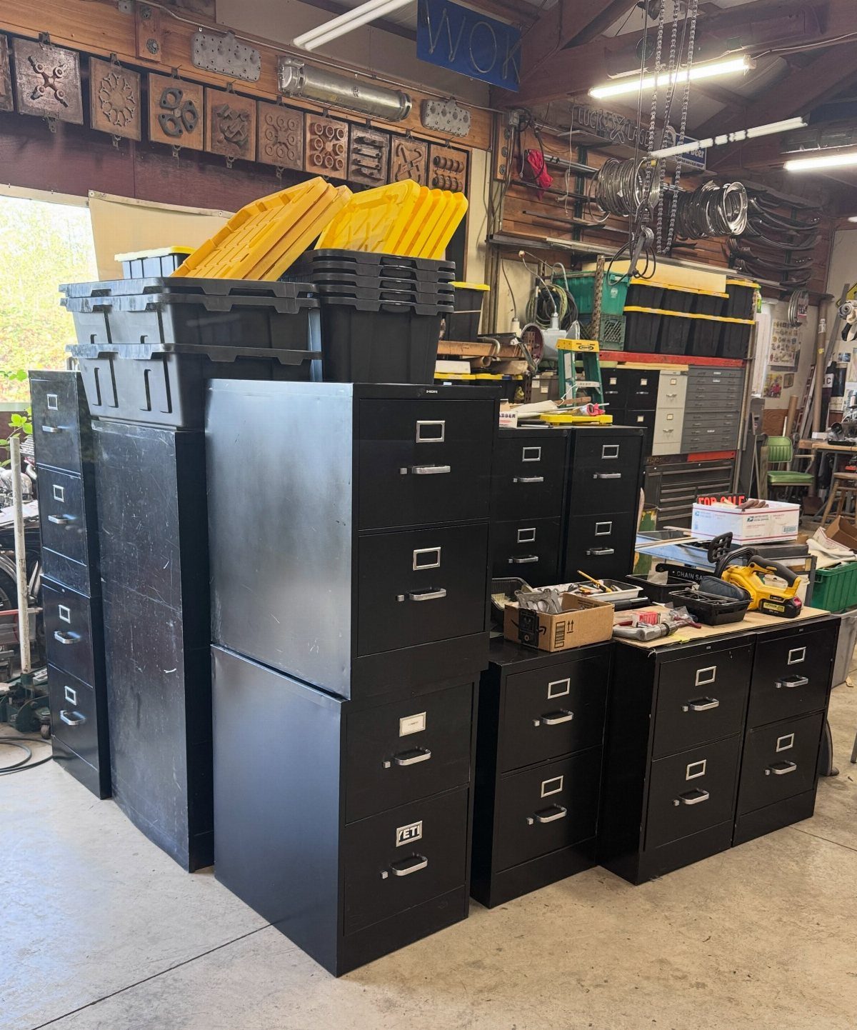 Black metal file cabinets grouped together in a cluttered workshop with storage bins.
