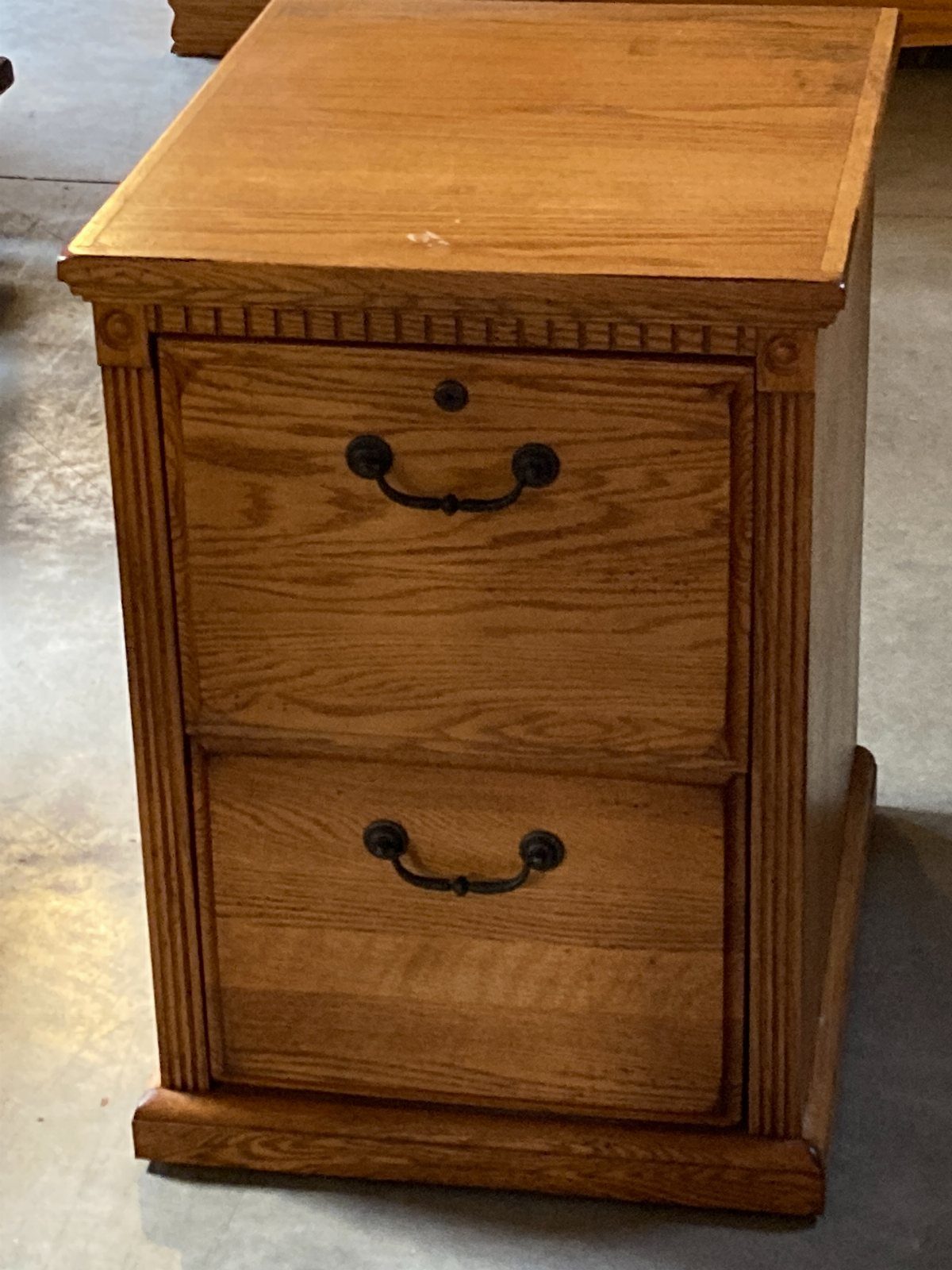 Wooden two-drawer file cabinet with black handles and fluted side detailing.