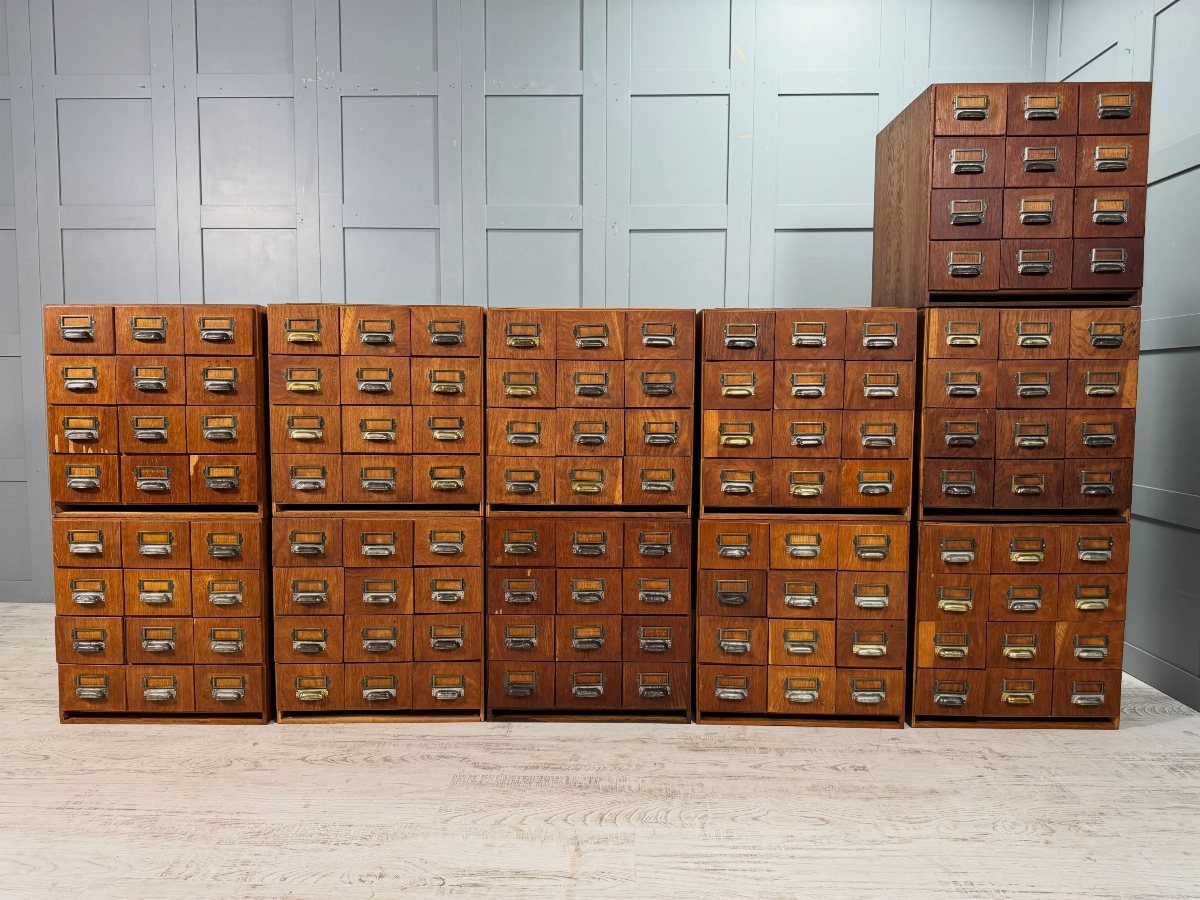 Vintage wooden card catalog cabinets with small drawers against a grey paneled wall.
