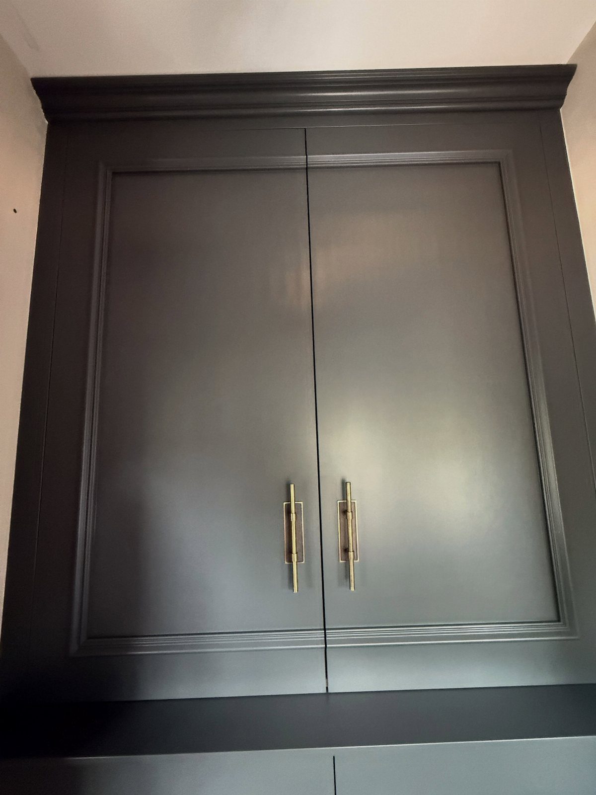 Dark grey painted cabinet with gold handles and decorative molding against white wall