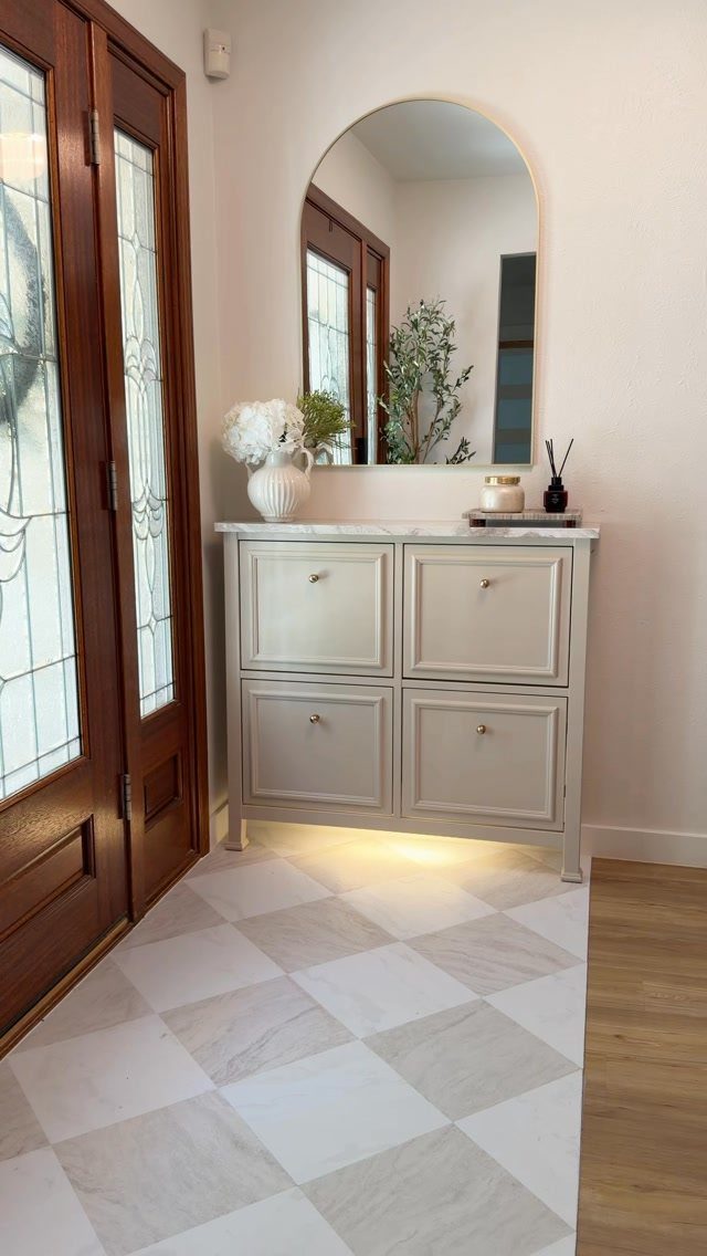 White modified shoe cabinet with marble top and arched mirror in an entryway