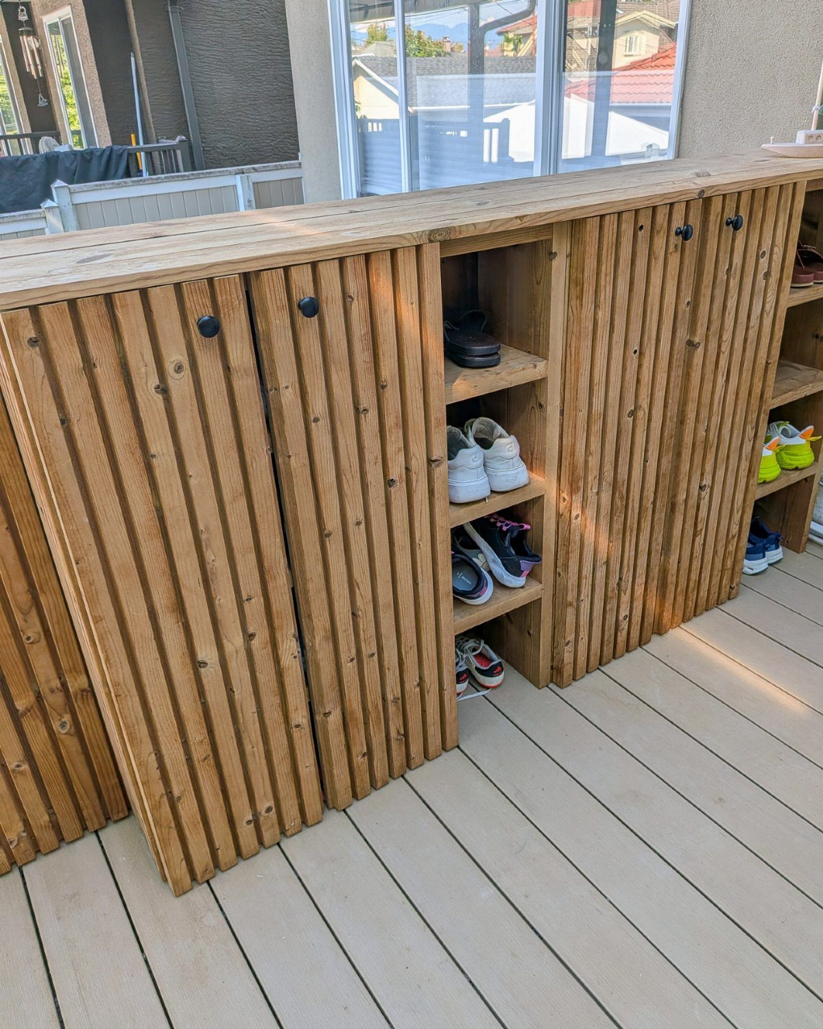 Fluted wooden shoe cabinet with open shelving on a light-colored outdoor deck