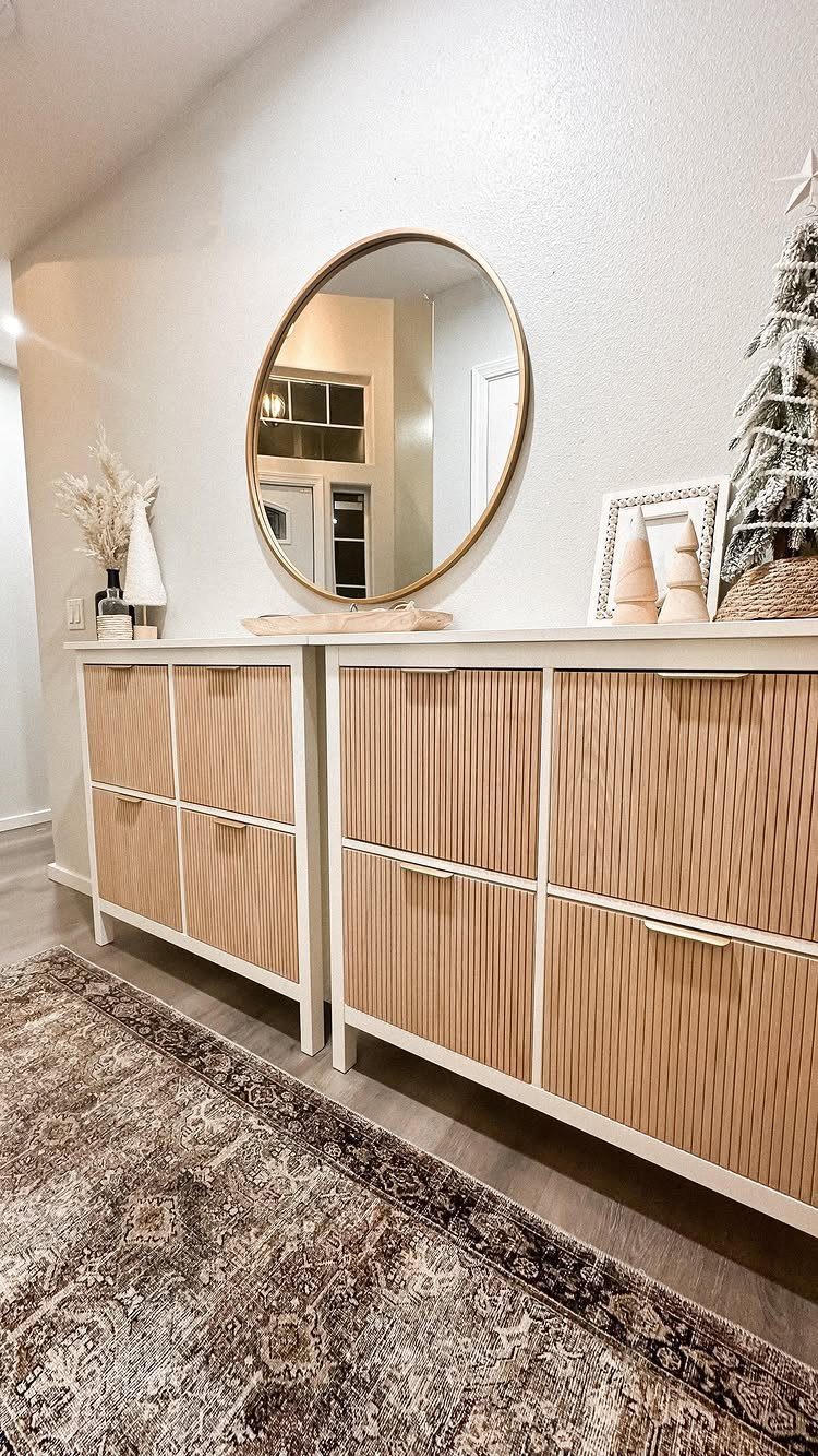 White shoe cabinets with ribbed wood panels, a round mirror, and a patterned rug.