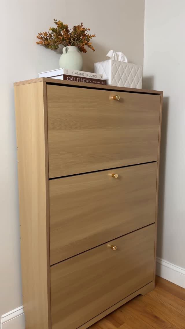 Light wood shoe cabinet with gold knobs and decorative items on top.
