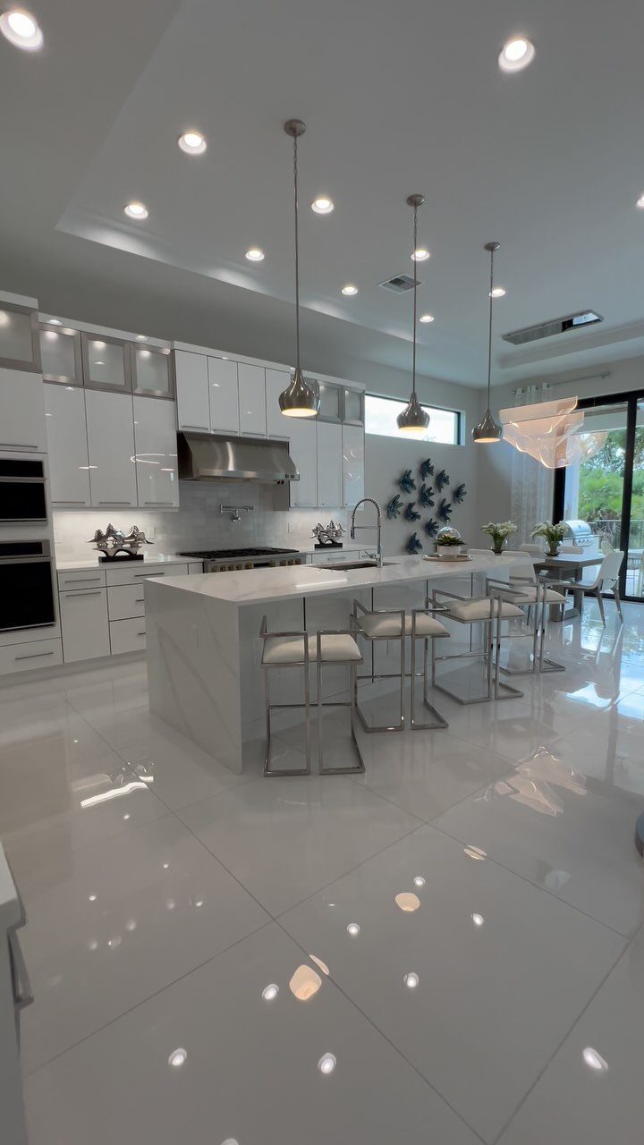 Modern white kitchen with a marble island, silver barstools, and glossy white cabinetry.
