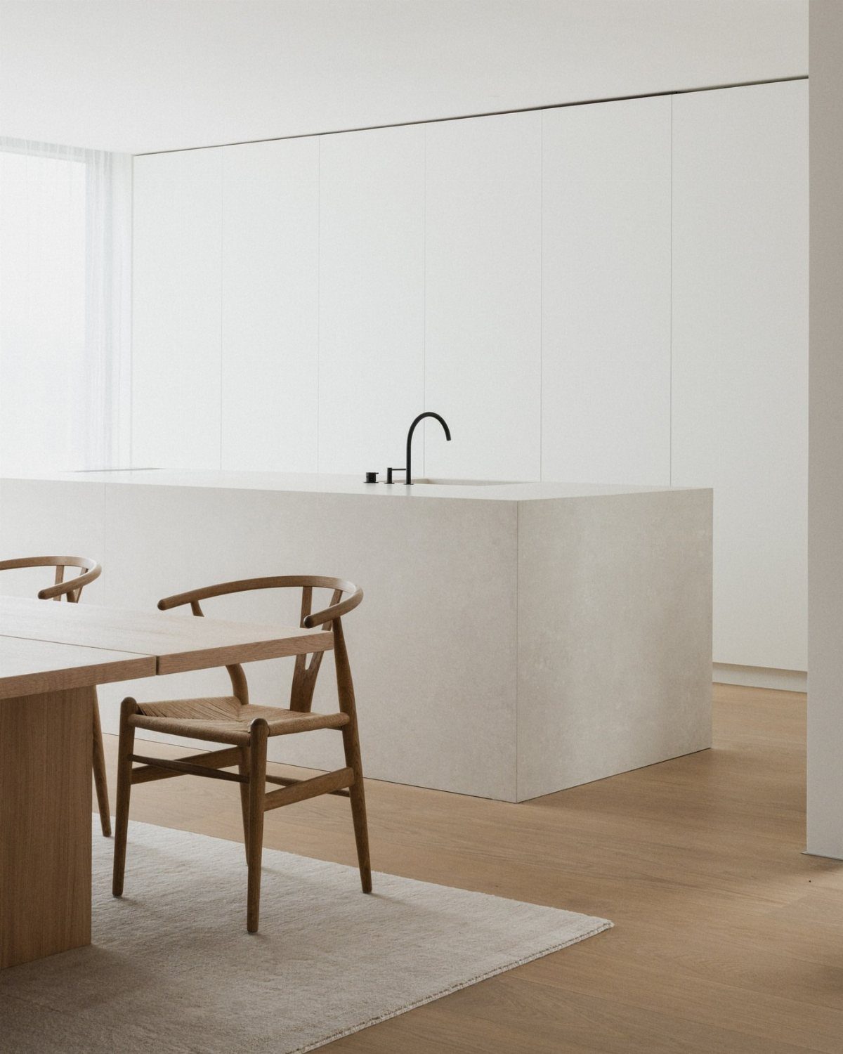 Minimalist white kitchen with seamless cabinetry and a stone island with black faucet.