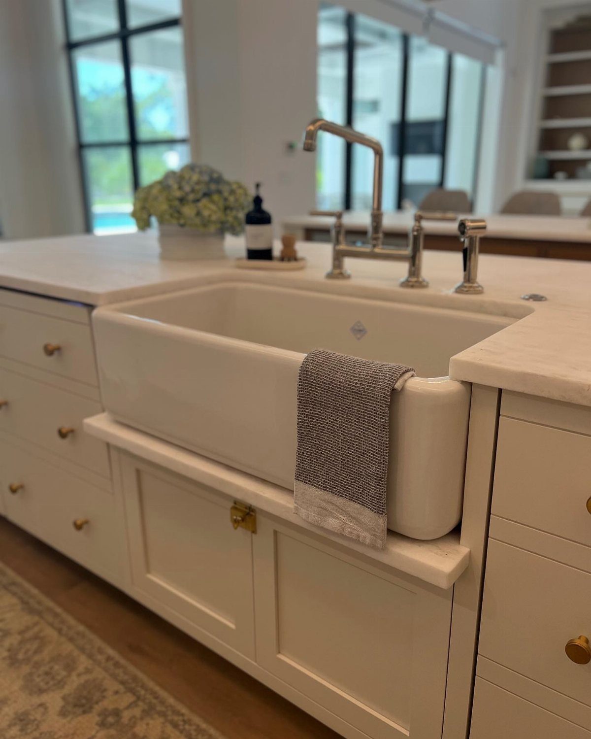 White farmhouse sink with silver faucet and marble countertop in a bright kitchen.