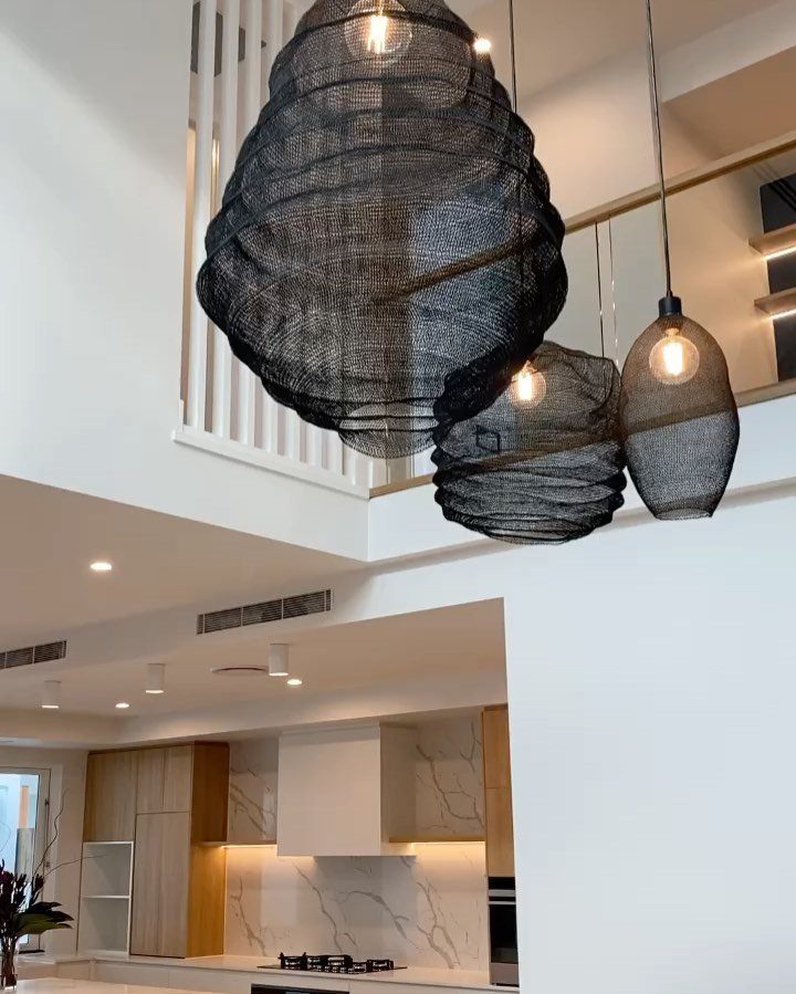 Modern kitchen with light wood cabinetry and large black woven pendant lights.