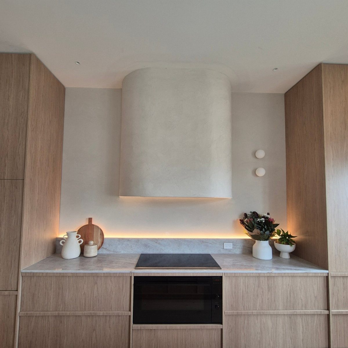 Curved plaster range hood in a modern kitchen with light wood cabinets.