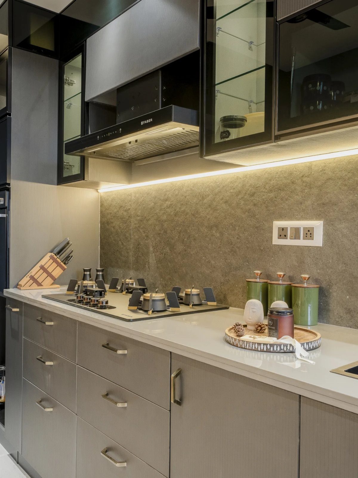 Grey stone textured backsplash in a modern kitchen with under-cabinet lighting and grey cabinets.